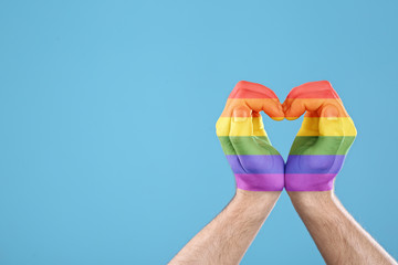 Man making heart with hands painted in LGBT flag on color background, closeup and space for text. Gay community