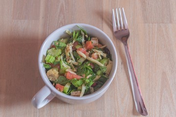 White bowl of colorful salad on table top with steel fork