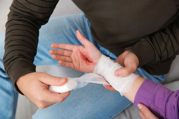 Young man applying bandage on woman's injured hand at home, closeup. First aid