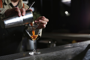 Fototapeta na wymiar Barman pouring martini espresso cocktail into glass at counter, closeup. Space for text