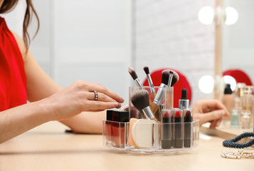 Woman reaching for organizer with cosmetic products and makeup accessories on dressing table indoors, closeup
