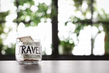 Glass jar with money and word TRAVEL on table against blurred background, space for text