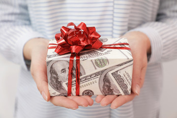 Woman holding gift box wrapped in dollars, closeup