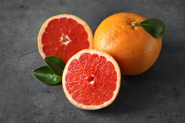 Fresh tasty grapefruits with leaves on grey table