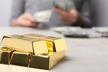 Stacked gold bars and woman counting money at table, closeup. Space for text