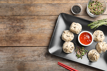 Flat lay composition with plate of tasty baozi dumplings, sprouts, sesame seeds and sauce on wooden table. Space for text