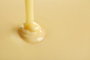 Tasty pouring condensed milk as background, space for text. Dairy product