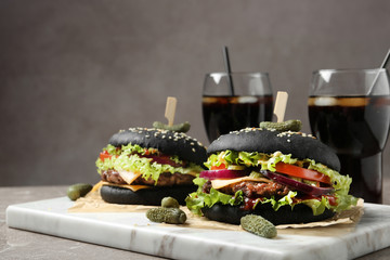 Board with black burgers and drinks served on table