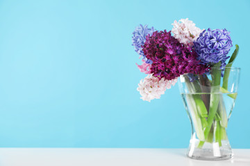 Beautiful hyacinths in glass vase on table against color background, space for text. Spring flowers