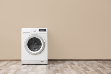 Modern washing machine with laundry near color wall, space for text