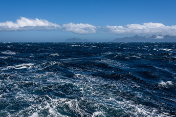 View of Atlantic Ocean and distant mountains, choppy water, calm blue sky with white clouds