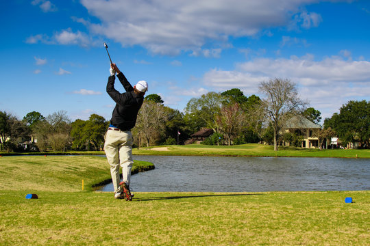 Amateur Golfer Finishing His Swing with ball heading towards the pin hole over water - Powered by Adobe