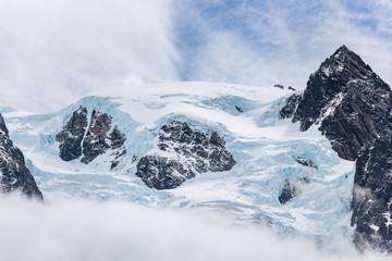 Fototapeta na wymiar Snow and glacier ice covered rocky mountain peak, with fog below and light white clouds in a blue sky above, Drygalski Fjord, South Georgia