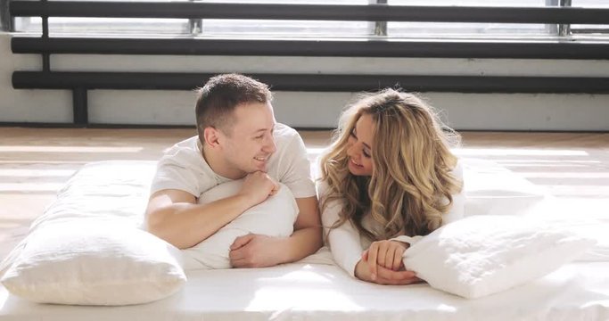 Couple in love in bed are looking at camera and smiling. Man is kissing his girlfriend gently on the forehead. Love relationship concept.