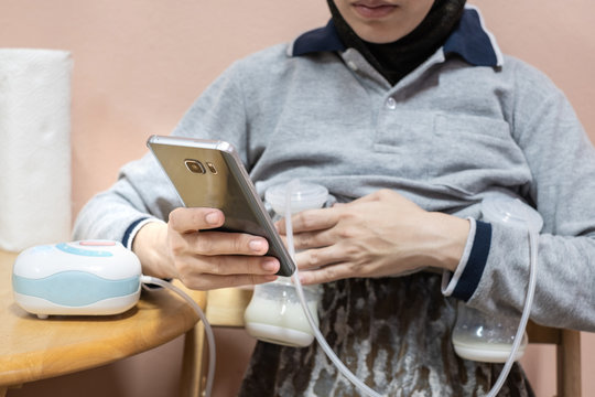 Busy Mother Pumping Breastmilk With Automatic Breast Pump Machine While Using Mobile Phone.