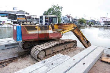 An excavator loader machine and concrete piles on pontoon floating in river for riverside construction work