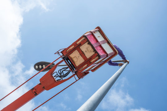 Technician on bucket truck high up of a crane to fix street light.