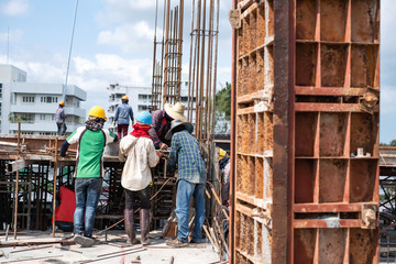 Workers collaborating in the installation of cement formwork frames at construction site.