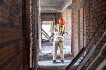 Asian architect or engineer holding project blueprint papers and write on it. He wear helmet at construction site.