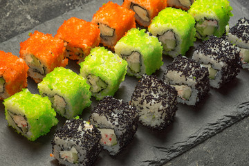 Set of assorted japanese sushi food on a black stone plate, close up angle view. Rolls with tuna, salmon, shrimp, crab and avocado. Sushi menu.
