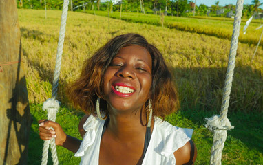young happy and beautiful black African American woman in Summer dress playing outdoors on swing...