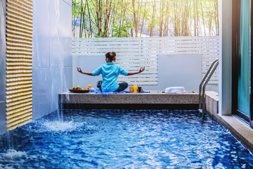 Girl doing yoga fitness exercise for relax and meditation at poolside Inside in the house,during meditation with a orange juice and fruit, apples, oranges placed on the side.