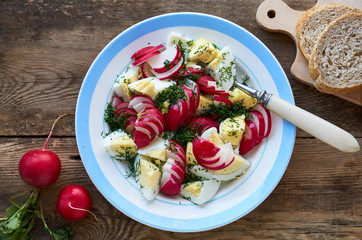 Vegetable salad with radishes, dill and eggs on a wooden background