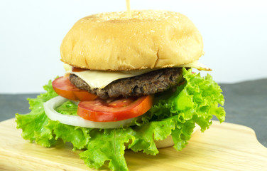 Burger beef cheese in a Chopping Wood props decoration with Green salad, tomato and sausage Rust stone wall on background, Copy space..