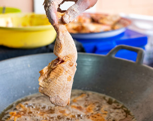 Close-up of hand holding and putting batter chicken drumstick into hot pan with cooking oil to fry.