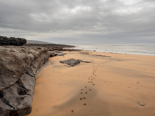 Beach in county Clare, Burren area, transition between sand and stone beach. cloudy day, gray clouds in the sky, animal footprint on the sand. 