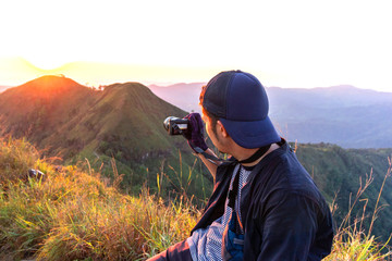 Thai young hiker taking photo of amazing sunset landscape on peak mountain at Khao Chang Puak national park in Kanchanaburi province, Thailand.