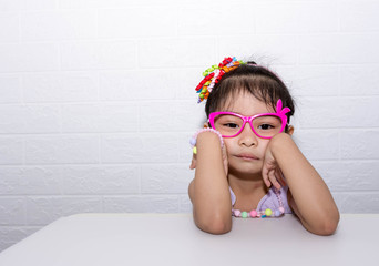 Female asian child girl posing wacky sad lonely pose while wearing some accessories like crown, necklace, pink eye glasses and wearing purple dress