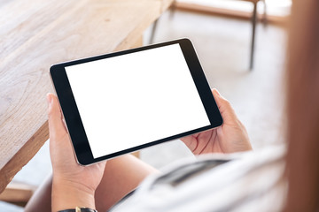 Mockup image of a woman sitting and holding black tablet pc with blank white desktop screen horizontally