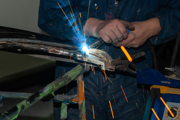 Close-up view strong man is a welder in blue working overalls without gloves on arms, a metal...