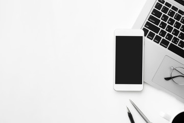 Smartphone with blank mock up screen is on top of white office desk table with laptop computer and...