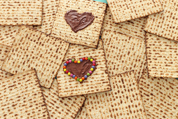 Pesah celebration concept (jewish Passover holiday) with chocolate heart and colorful candies over matzah. Top view flat lay