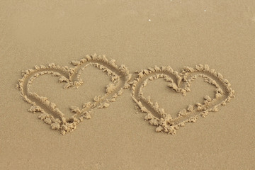 Two hearts drawn in the sand on the beach.