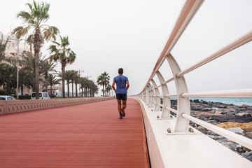 A man runs along a beautiful promenade with a white fence.