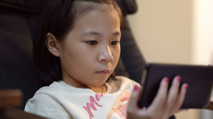 Closeup little asian girl playing with smart phone .