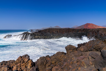 Fototapeta na wymiar Spain, Lanzarote, Rough atlantic sea in los hervideros cove next to red volcanoes