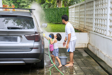 Two children and their father wash a car at home
