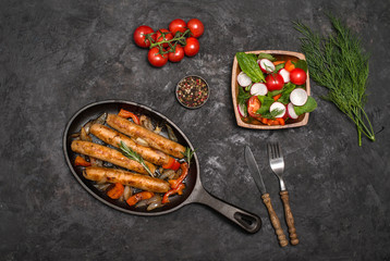 Sausages on the grill pan on the wooden background. Top view. Frying pan with fried sausage, vegetables and fork and knife on a rustic wooden table.