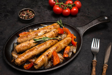 Sausages on the grill pan on dark background close-up. Side view. Frying pan with fried sausage, vegetables and fork and knife on a black wooden table.