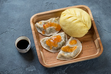 Wooden serving tray with korean steamed potstickers and a pigodi bun, studio shot on a blue stone surface