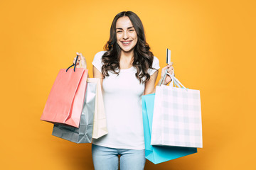 Buy in sales. Beautiful girl with long dark and curly hair, eye catching smile and sporty body shape is holding a lot of shopping bags with her new things in it and smiling because of pleasure.