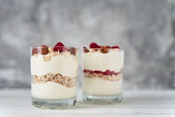 Two glasses of greek yogurt granola with raspberries, oatmeal flakes and nuts on a white background. Healthy nutrition