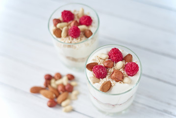 Two glasses of a greek yogurt granola with raspberries, oatmeal flakes and nuts, top view. Healthy nutrition