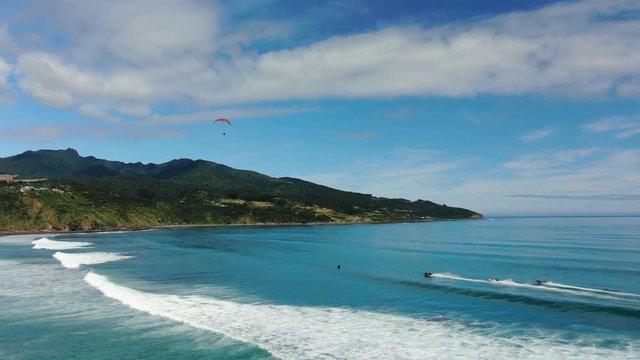 Orbiting drone footage of a paraglider in flight above the ocean as speed boats are racing underneath. 4k video