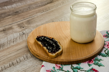 jar of milk, bread spread with jam, on a wooden board
