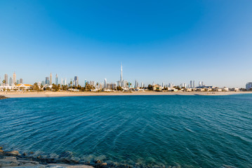 Naklejka premium Futuristic Skyscraper buildings view from rock beach island with blue waterfront and blue sky background